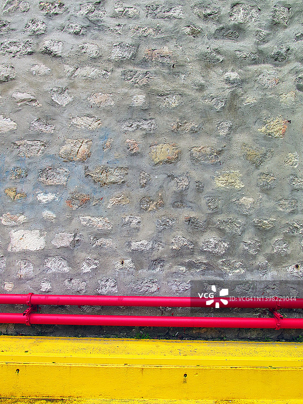 巴黎：风化的灰色粗糙石墙与黄色混凝土底座和红色管道图片素材