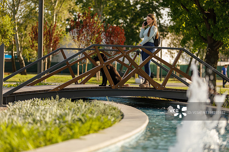 年轻女子在公园桥上打电话图片素材