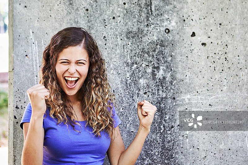 欢笑着，兴奋地挥拳庆祝的年轻漂亮女人：她是个赢家！图片素材