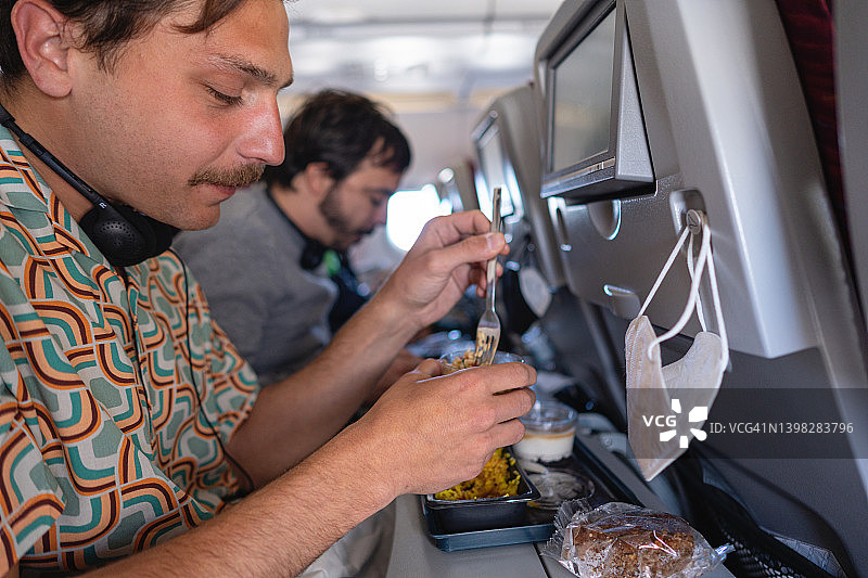 旅行途中在飞机上用餐的年轻白人男游客图片素材