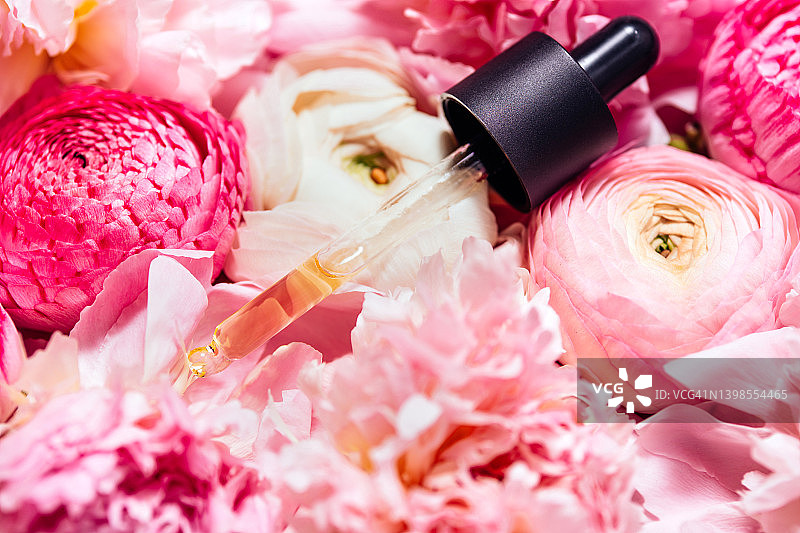 带有聚谷氨酸的面部精华玻璃滴管，置于淡粉色牡丹和毛茛花上（精美设计背景，宏观俯视摄影）图片素材