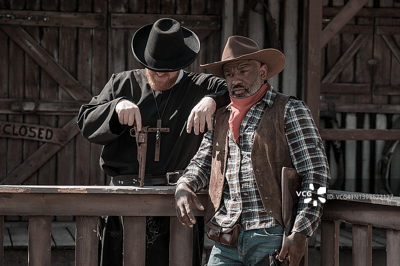 帅气黑人牛仔与牧师在狂野西部背景中图片素材