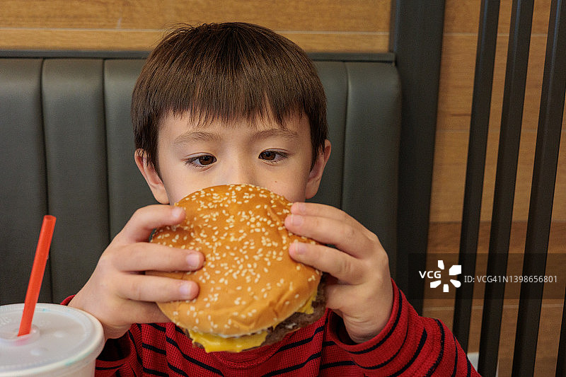 在快餐店吃汉堡的学龄亚洲男孩图片素材
