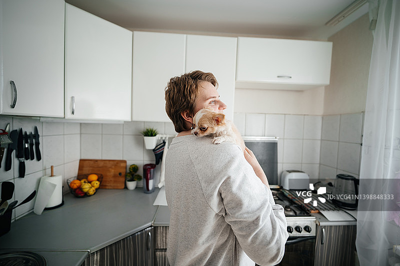 癌症缓解期妇女在家中厨房拥抱小狗，充满喜悦。癌症患者与家庭互相扶持概念图片素材