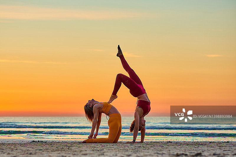 两个女人在日出时在海滩上做瑜伽图片素材