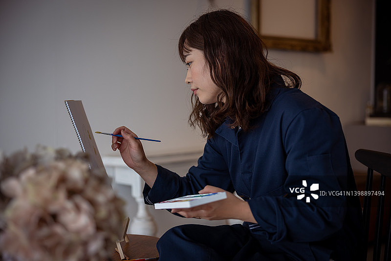 女人在她的工作室里在画布上绘画-侧视图图片素材