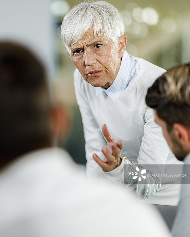 年长的女性CEO在办公室的会议上与同事争论图片素材