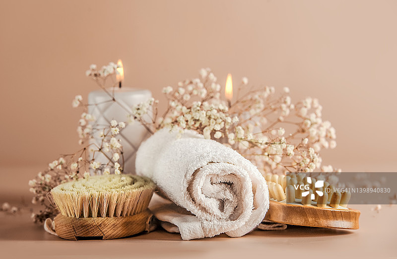 可持续的身体护理：干按摩刷、毛巾、蜡烛和鲜花在米色背景中图片素材