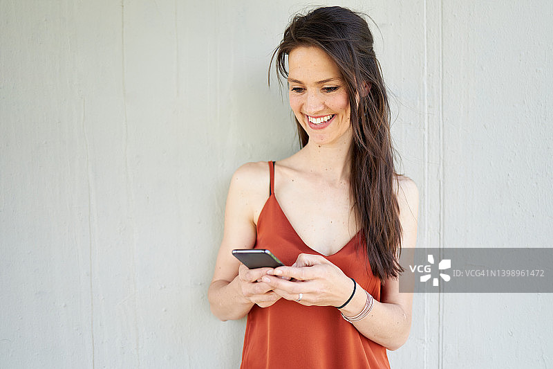 长着棕色头发的年轻女子笑着看智能手机图片素材