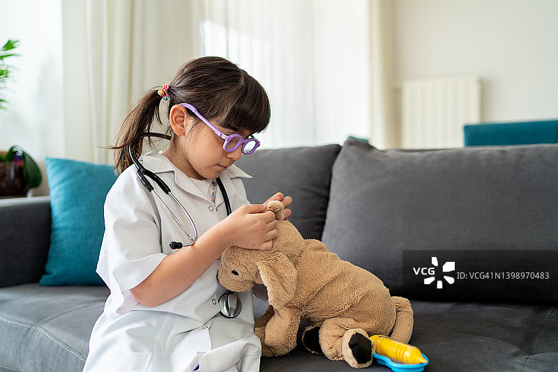 穿医生服的小女孩用玩具听诊器检查玩具狗图片素材