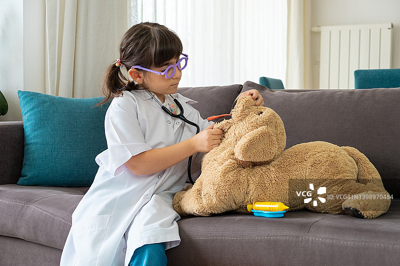 穿医生服的小女孩用玩具听诊器检查玩具狗图片素材