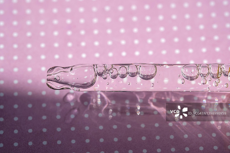 滴管吸取含有气泡的化妆品凝胶或精华液，紫色背景图片素材