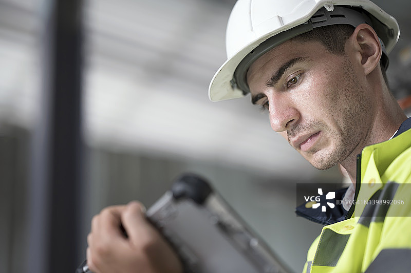 制造业大数据安全：男性生产工程师使用平板电脑访问工厂生产过程数据图片素材