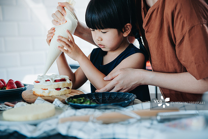 亚洲母亲和小女儿在厨房烤蛋糕，用草莓和奶油一起装饰，DIY生日庆祝图片素材