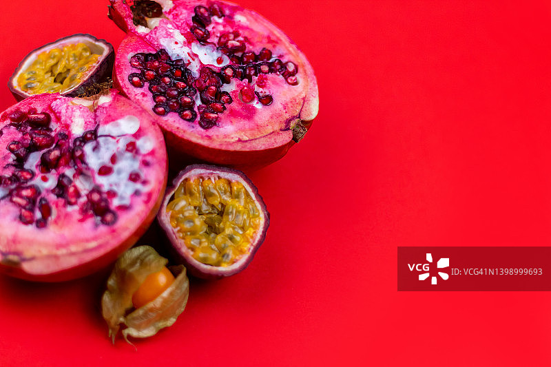 红色背景上的半个石榴、冬季樱桃和百香果图片素材