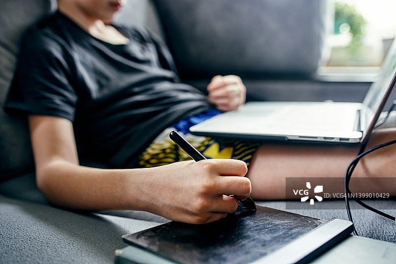 男孩坐在沙发上，拄着拐杖，用笔记本电脑和绘图板图片素材