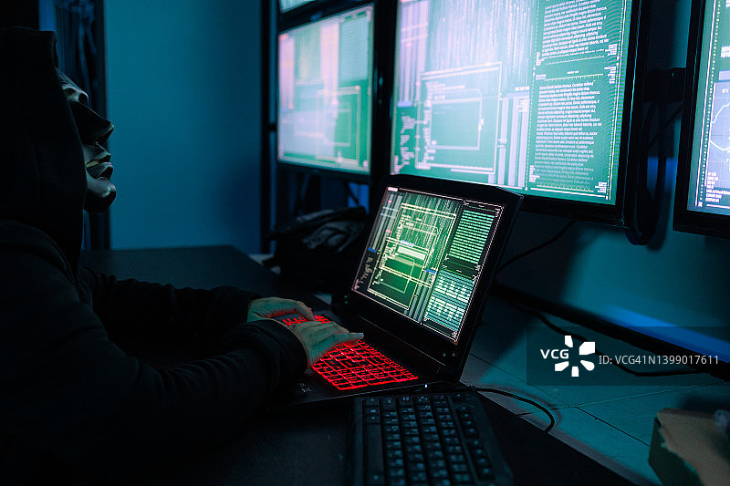 在黑暗房间里，戴着黑色面具的女人正在使用多台显示器攻击互联网。图片素材