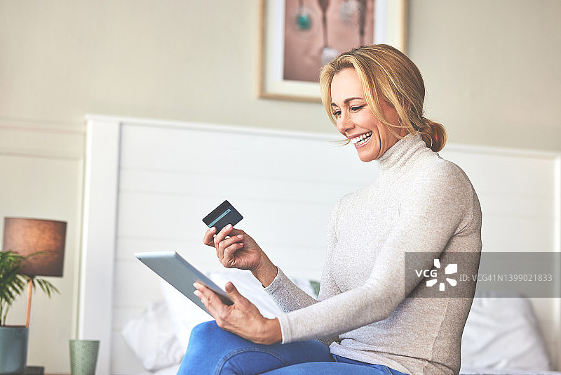 女人在家里的床上使用信用卡和数位板图片素材
