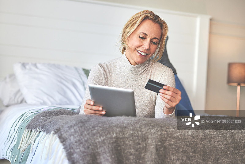 女人在家里的床上使用信用卡和数位板图片素材