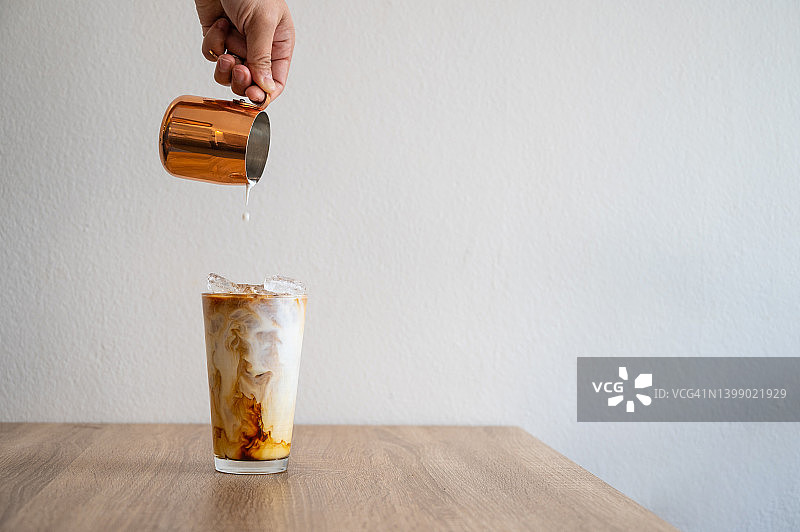 咖啡师将牛奶倒入冰咖啡中制作冰拿铁图片素材