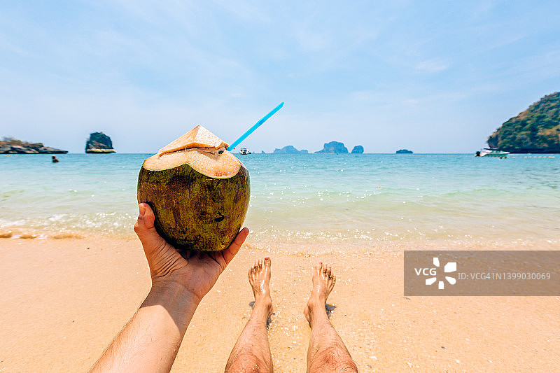 男人在海滩边放松身心喝新鲜椰奶，个人视角图片素材