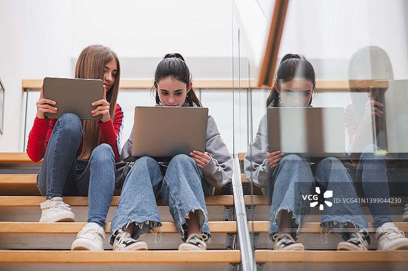 在高中楼梯上使用笔记本电脑和平板电脑的女孩图片素材