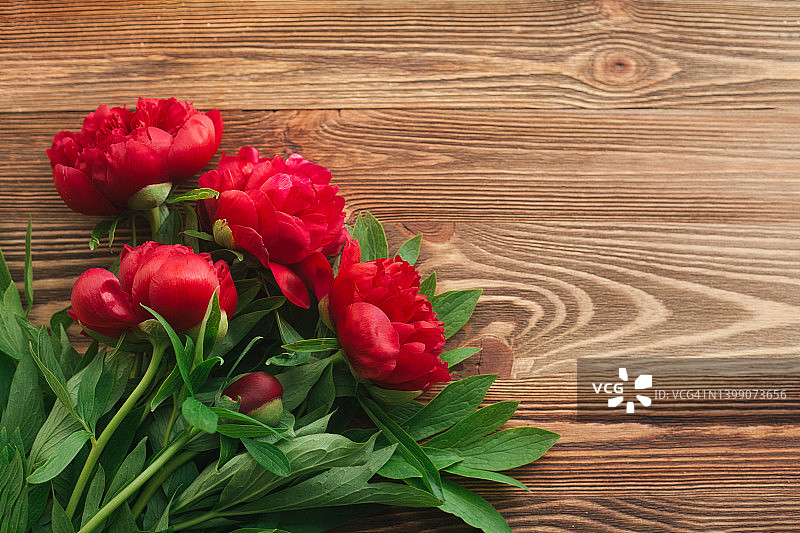 棕色木桌上的红色牡丹春季或夏季花卉，平铺俯视图。文本的复制空间。图片素材