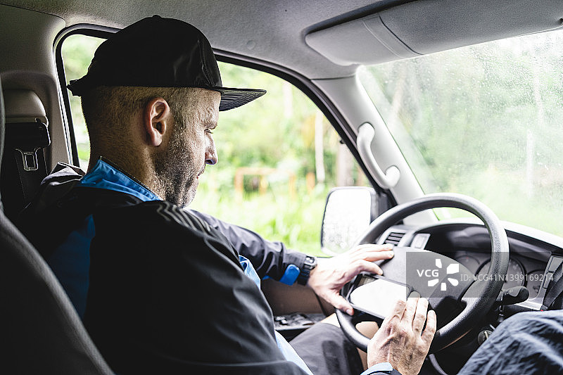 男人坐在车里，外面下着雨，使用手机图片素材