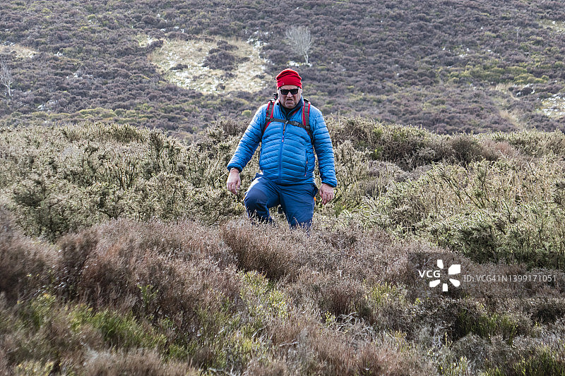 成年男子戴着帽子和太阳镜，脸上露出不高兴的表情;图片摄于英国威尔士登比郡克罗维德门和博德法里之间的奥法堤和克罗维迪安路国家步道。3月图片素材