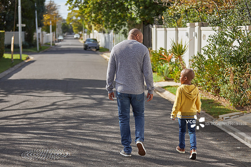 父子在街上行走。成熟男人和他的小男孩在路上轻松散步和交谈的后视图图片素材