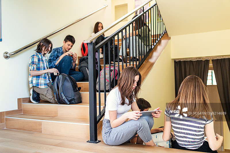 一群青少年学生坐在学校的楼梯上，准备上课图片素材