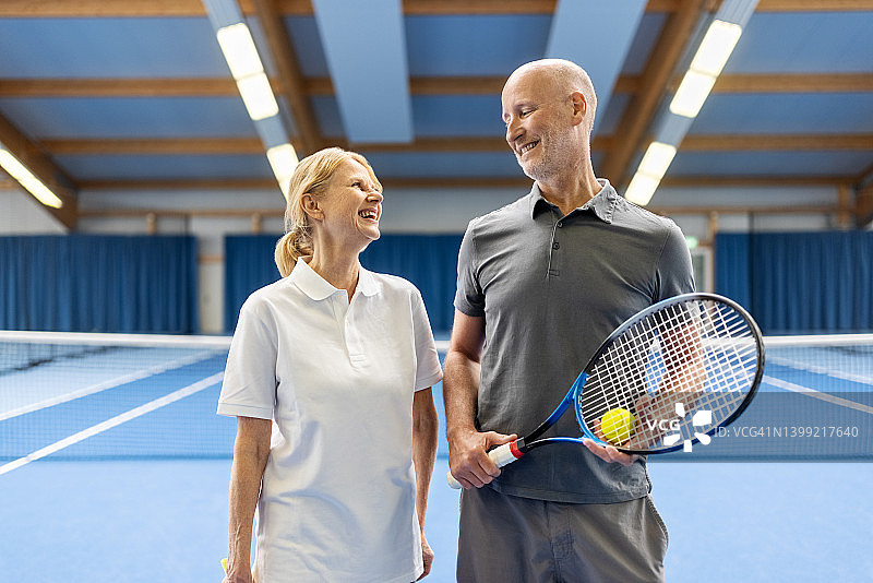 快乐的中年夫妇在室内网球场图片素材