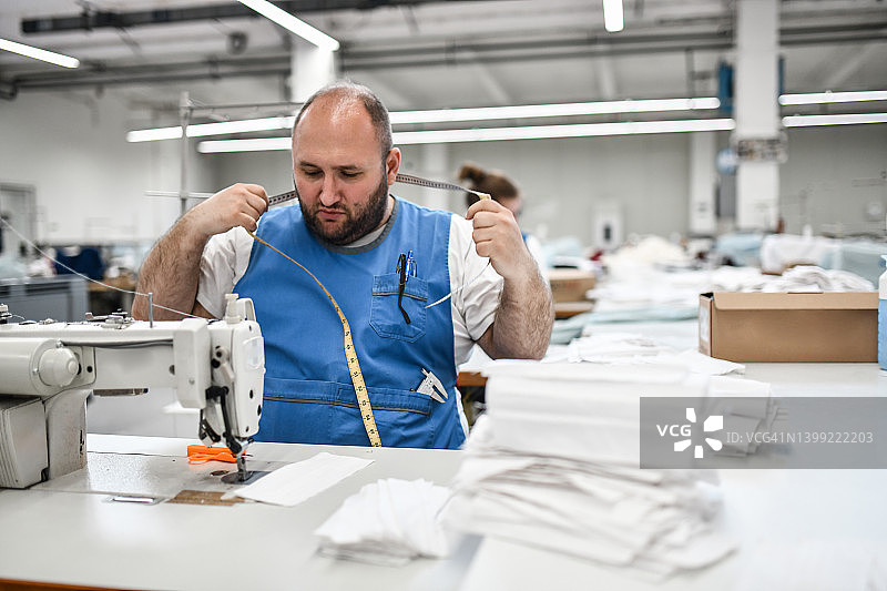 在纺织厂测量和缝制口罩的秃顶男子图片素材