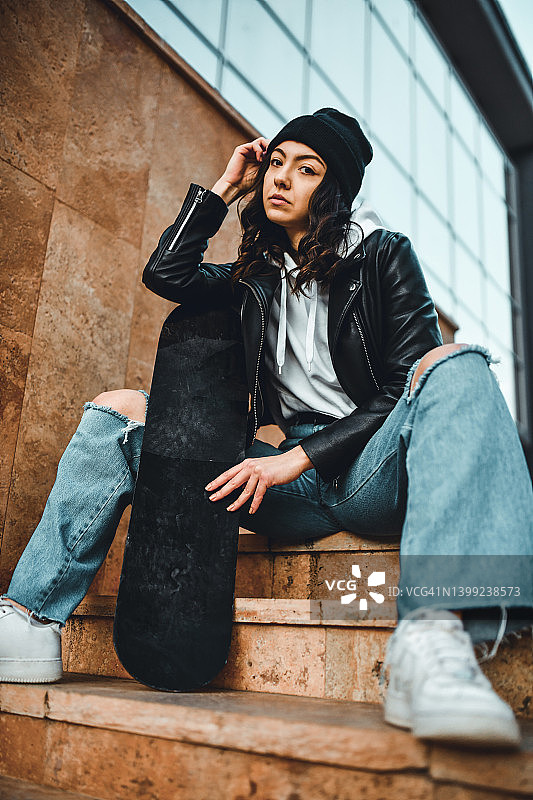 坐在室外楼梯上，手持滑板的严肃女性图片素材