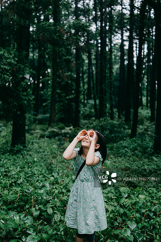 年轻女孩假装在森林里用双筒望远镜观察图片素材