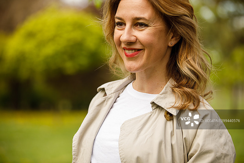快乐的中年妇女站在公园里，看向远方，微笑沉思预留空间照片图片素材