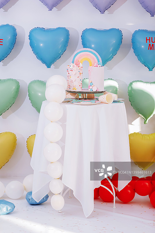 带有彩虹和彩色糖屑的大型生日蛋糕和彩色心形气球背景，生日派对，甜蜜假日图片素材