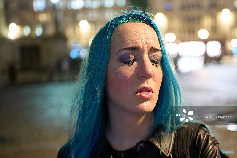 夜晚城市中一位情绪激动、哭泣的蓝发年轻女人的肖像图片素材