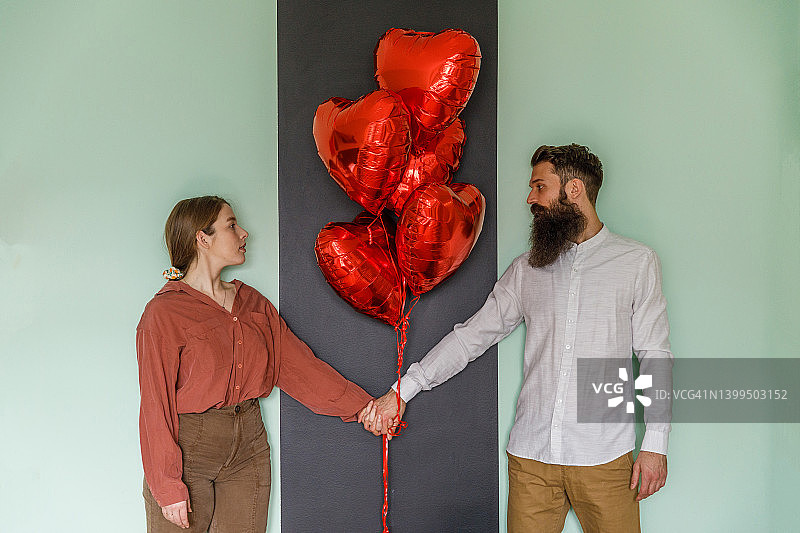 情侣站在墙边，手拿心形气球，深情对望图片素材