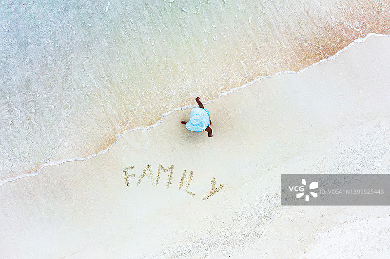 站在沙滩上“家庭”字样旁边的女人，俯视角度图片素材