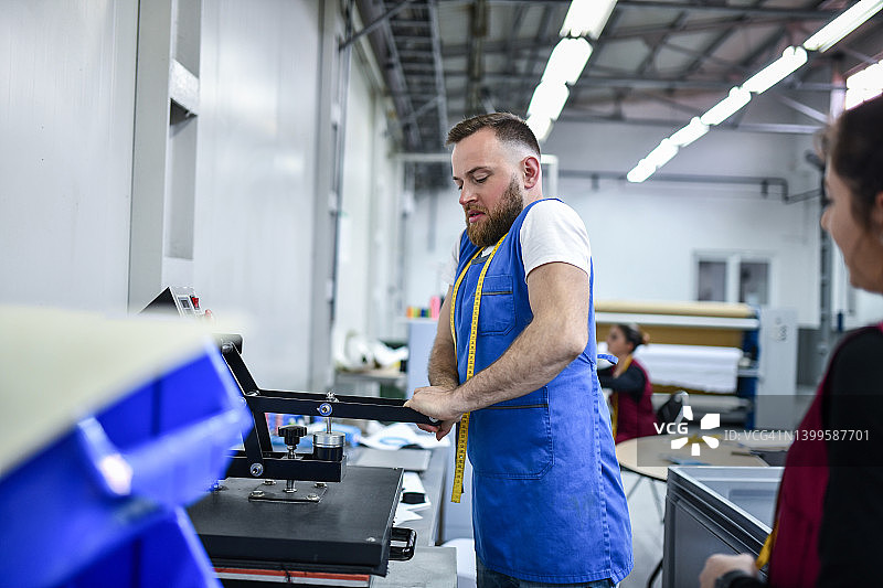 在纺织厂，男人在布料上使用印刷机图片素材
