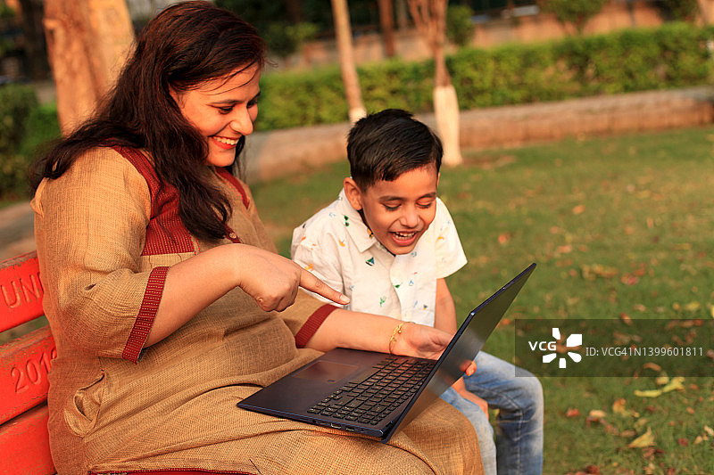 快乐的母亲和孩子在公园里使用笔记本电脑图片素材