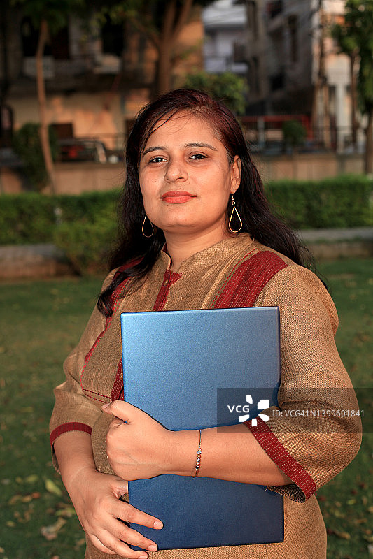 中年自信女性在户外手持笔记本电脑图片素材