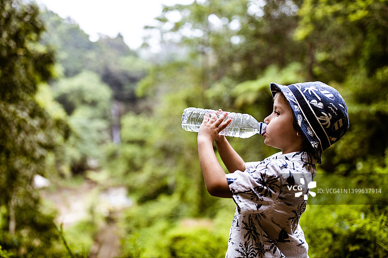 小男孩在大自然中饮水的侧面视图。图片素材