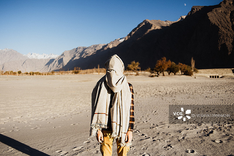 男人在喀喇昆仑山脉的冷卡特帕纳沙漠日落时分穿着普什图传统披肩图片素材