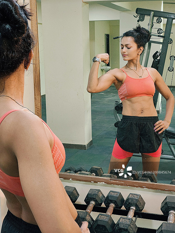 健美女性在健身房的镜子里看她的肱二头肌图片素材