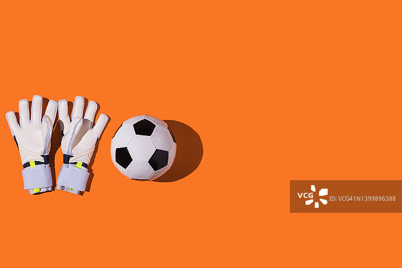 橙色背景上的白色守门员手套和足球，足球运动概念图片素材