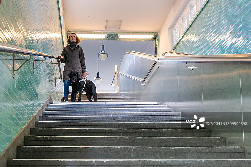 视力障碍的女人与导盲犬走下楼梯图片素材