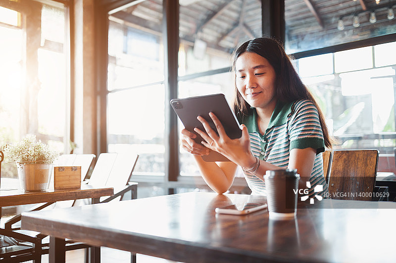 在复古咖啡馆使用平板电脑的休闲亚洲女商人图片素材