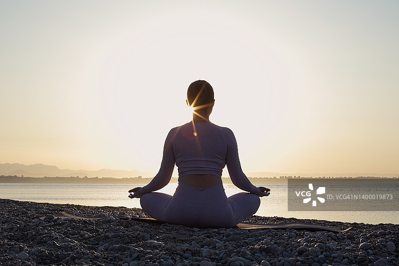 年轻女子在海边日出时冥想图片素材